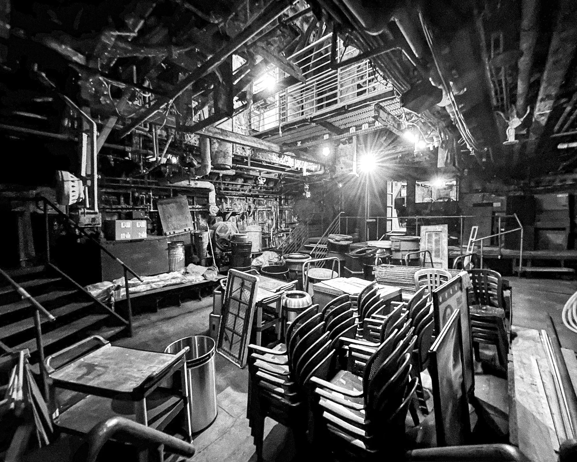 Backstage theatre area with stacked chairs and rigging, black and white