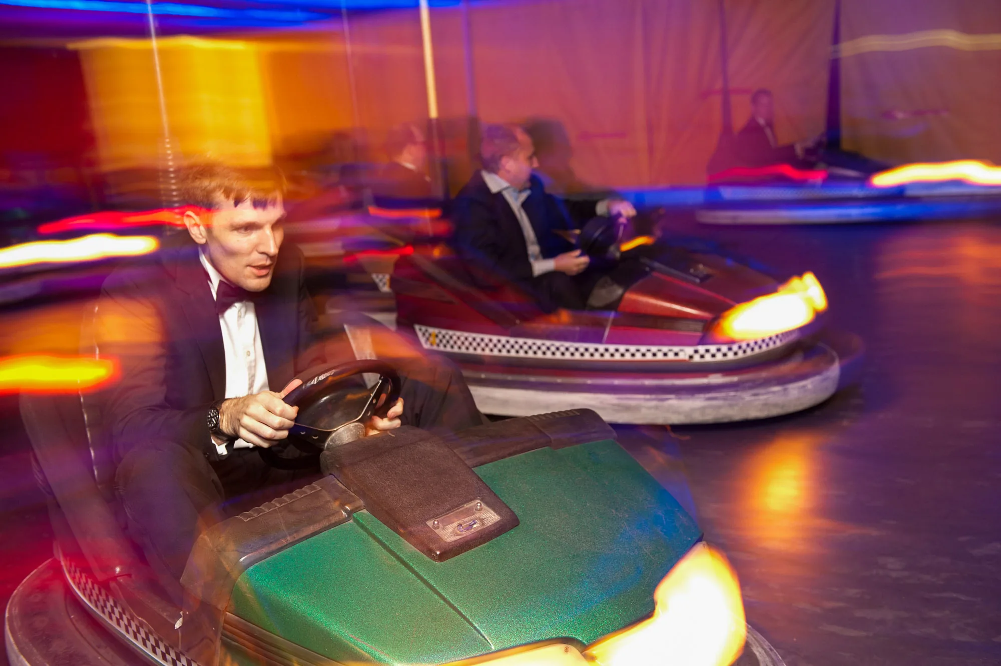Guests in black tie riding bumper cars at a corporate team event, corporate event photography by Hector's Eye