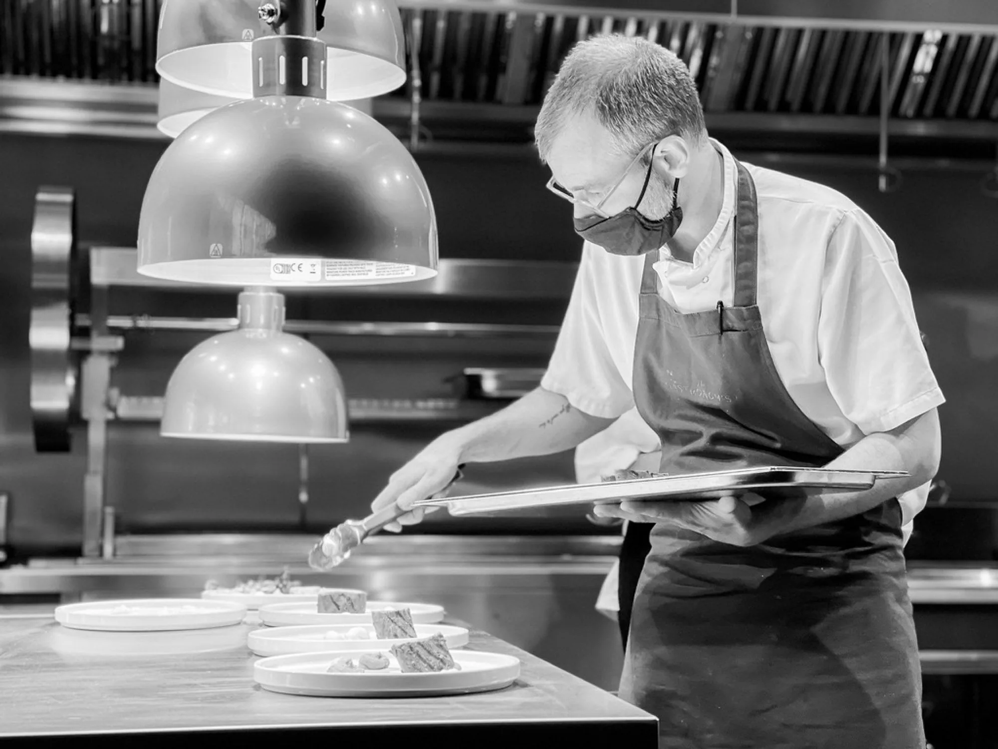 Chef carefully plating a dish in a professional kitchen, black and white brand storytelling photography by Hector's Eye