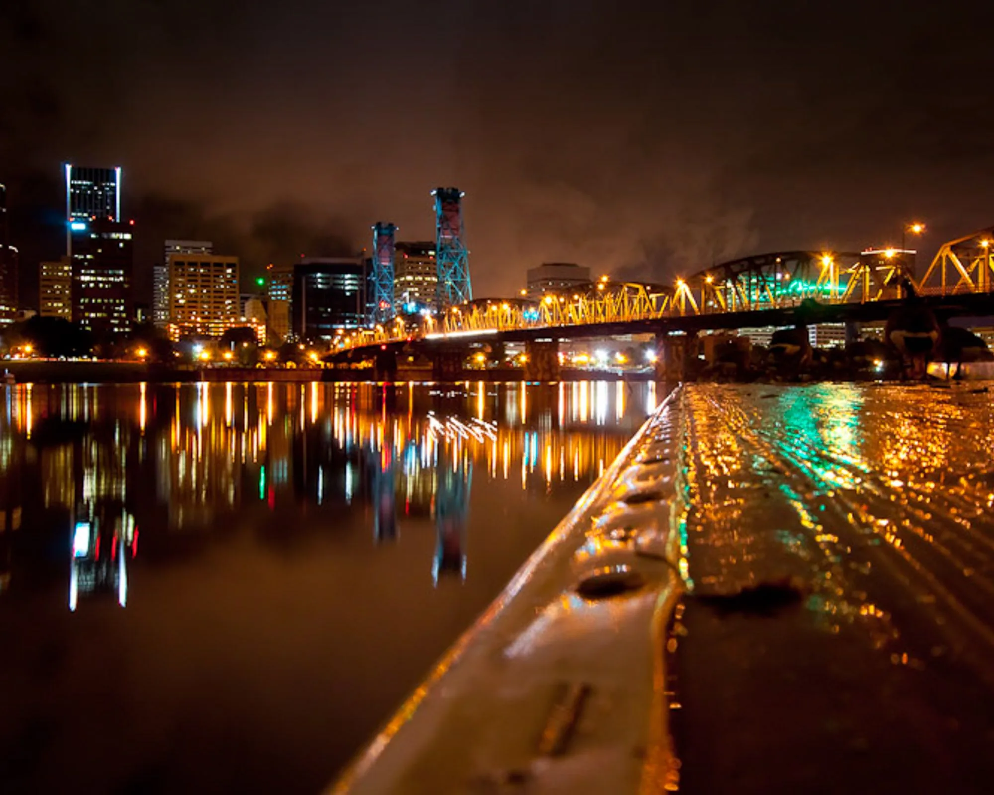 City skyline and steel truss bridge reflected in a river at night, landscape photography