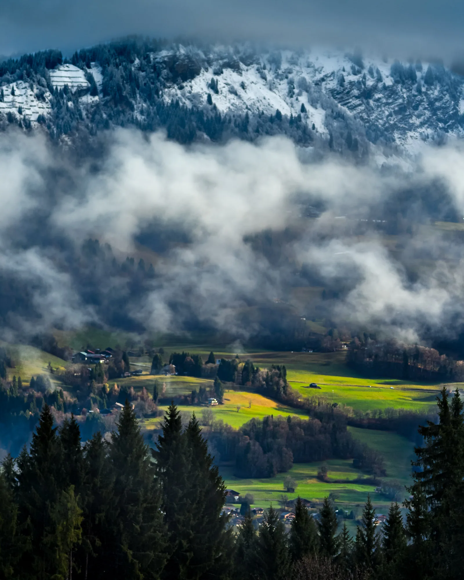 Cloud inversion rolling through a mountain valley beneath snow-capped peaks