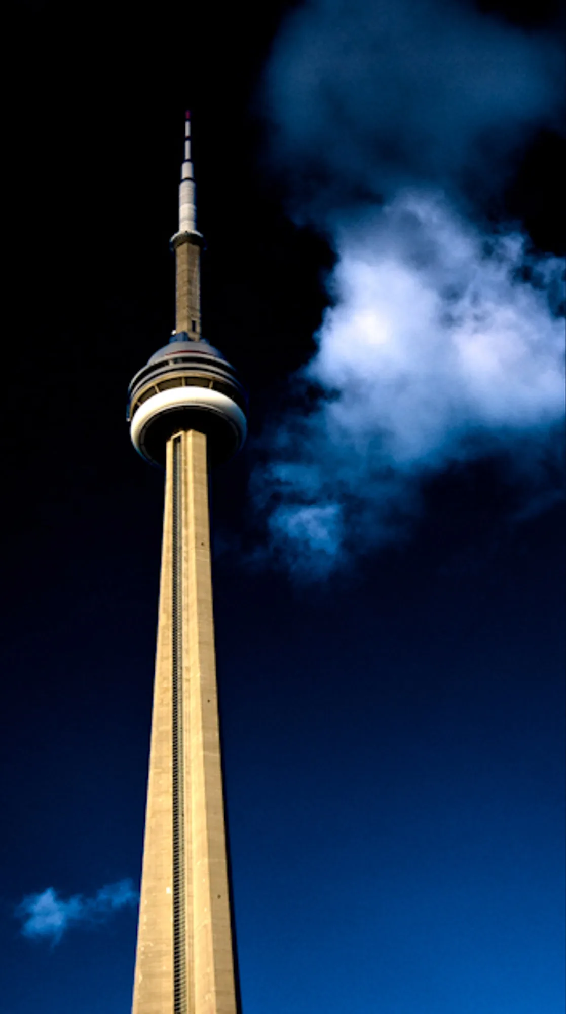 Toronto's CN Tower rising into a cloud against a deep blue night sky, architectural photography