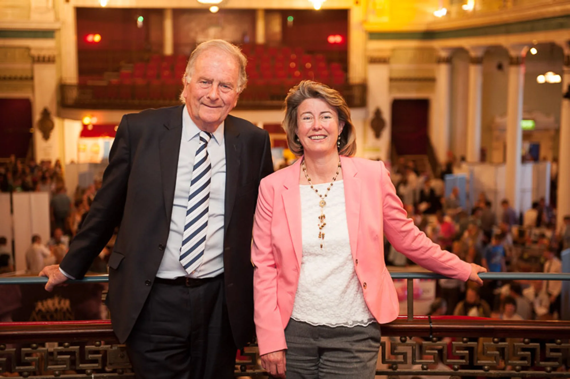 Two guests posing together on a balcony overlooking a busy conference hall, live event photography by Hector's Eye