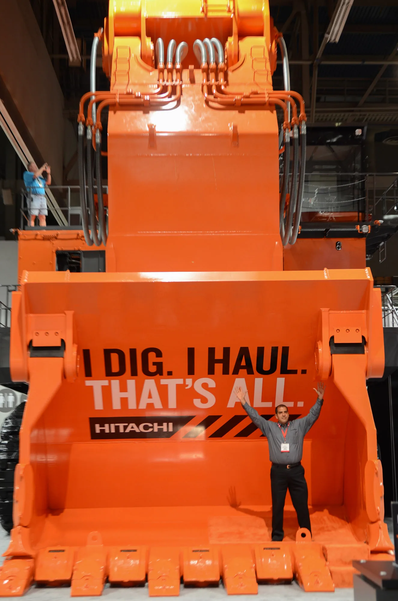 Visitor posing beneath a giant excavator bucket at a construction industry expo, corporate event photography by Hector's Eye