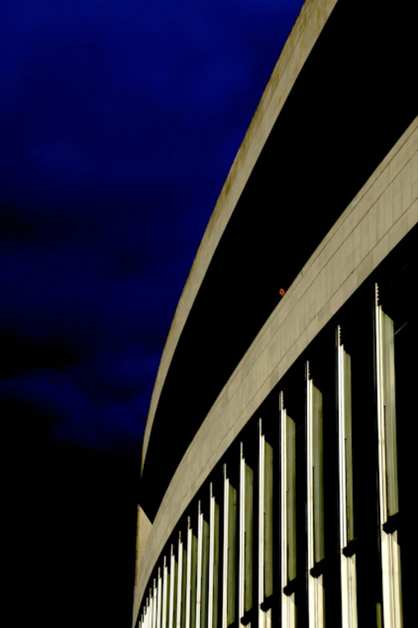 Curved illuminated building facade against a deep blue dusk sky, architectural photography