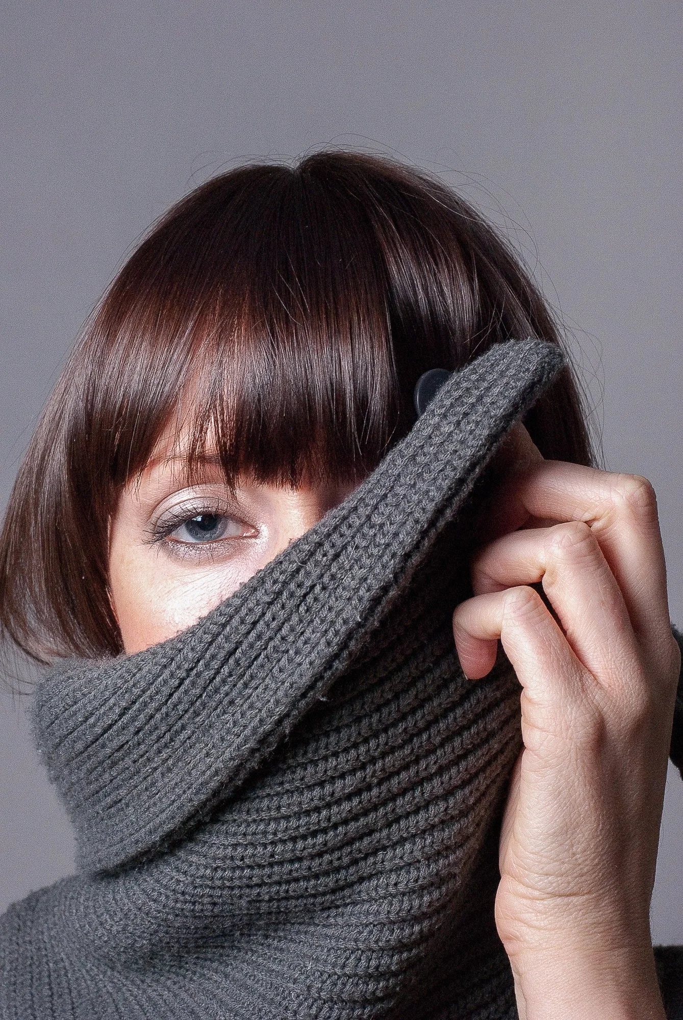 Editorial portrait of a woman with a grey knitted scarf pulled up to her eyes, studio portrait photography by Hector's Eye