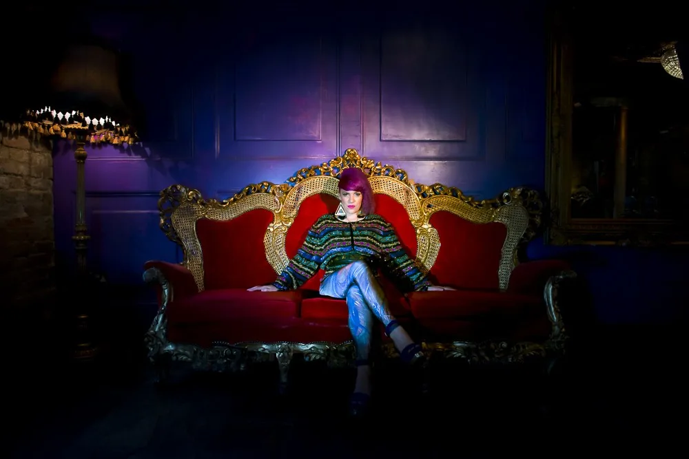 Full-length editorial portrait of a model with purple hair reclining on an ornate baroque sofa, styled portrait photography by Hector's Eye