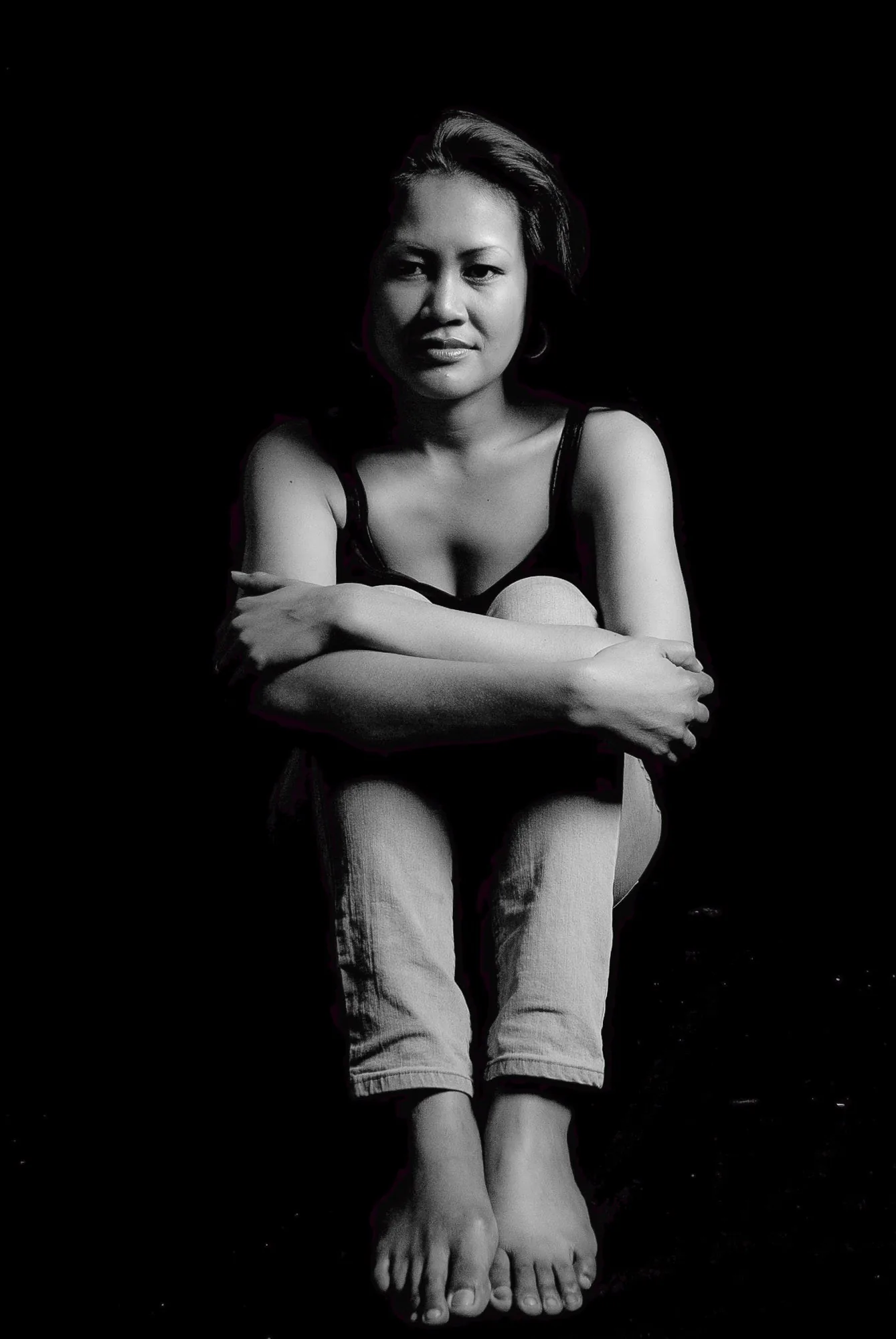 Black and white editorial portrait of a woman seated barefoot with arms wrapped around her knees, studio portrait photography by Hector's Eye