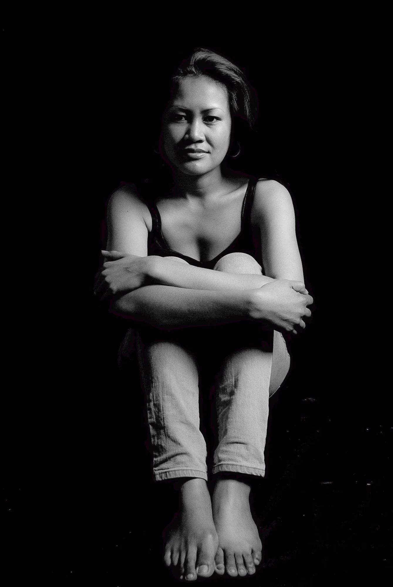 Black and white editorial portrait of a woman seated with arms wrapped around her knees, studio portrait photography by Hector's Eye