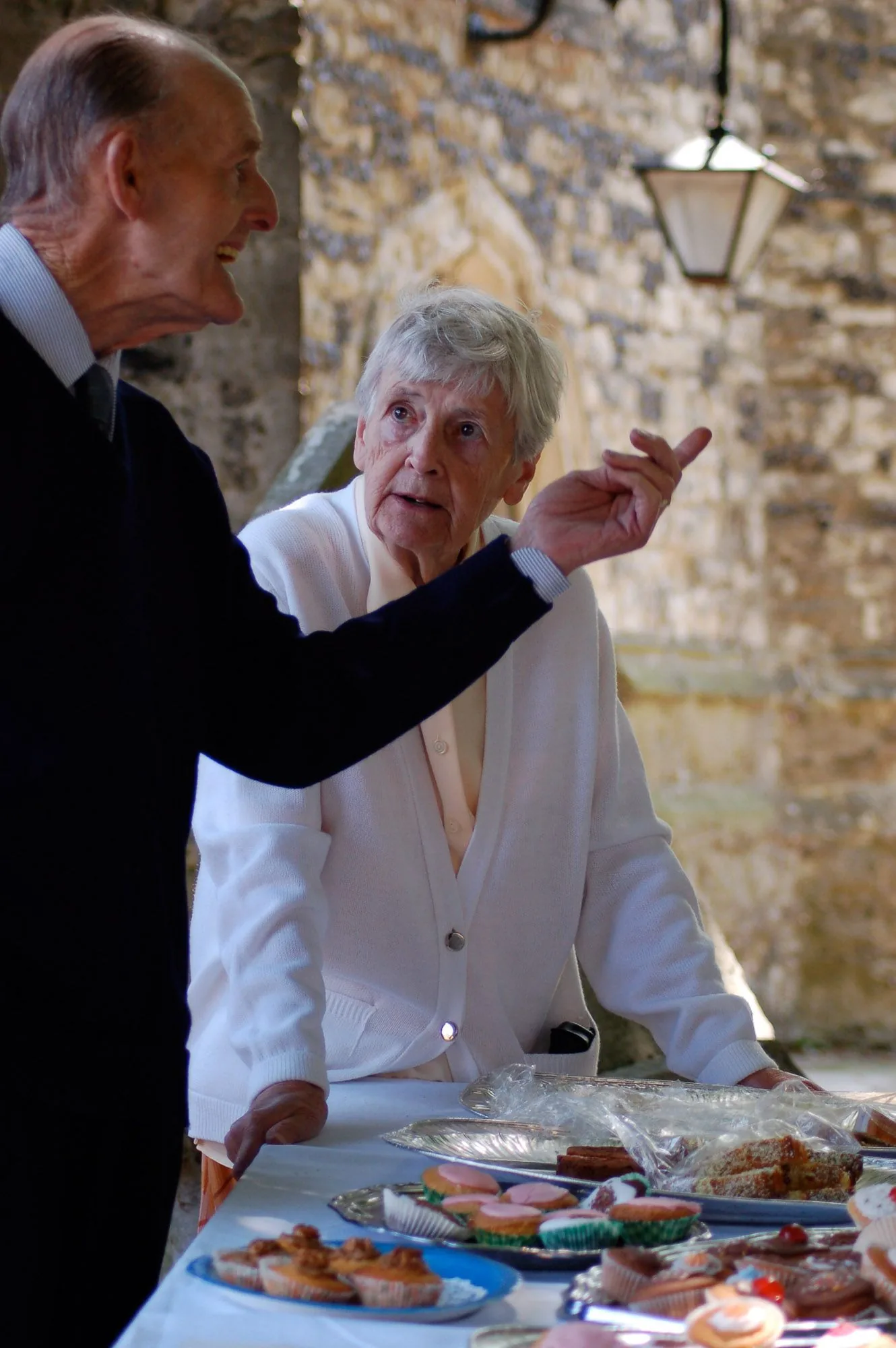 Elderly couple chatting animatedly at an outdoor community fete table, live event photography by Hector's Eye