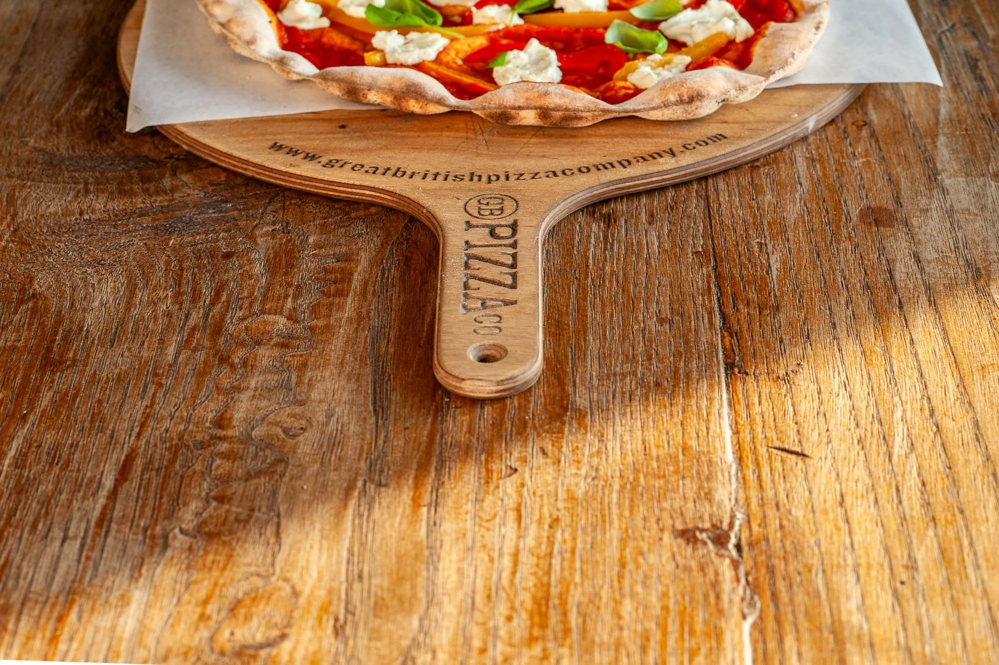 Wood-fired pizza with peppers, goat's cheese and basil on a branded GB Pizza Co. peel, food photography by Hector's Eye