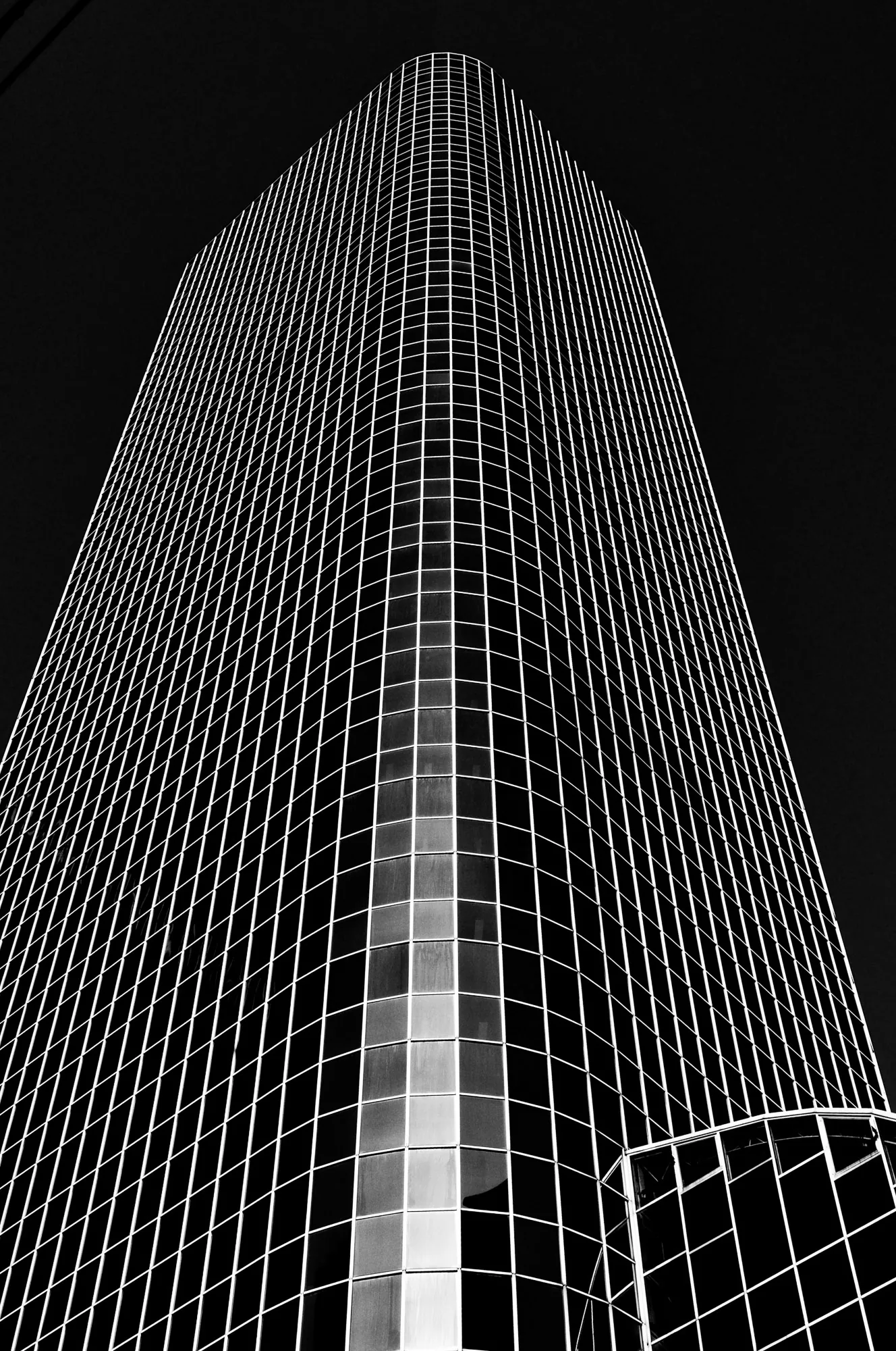 Looking up the grid-patterned glass corner of a skyscraper, black and white architectural photography