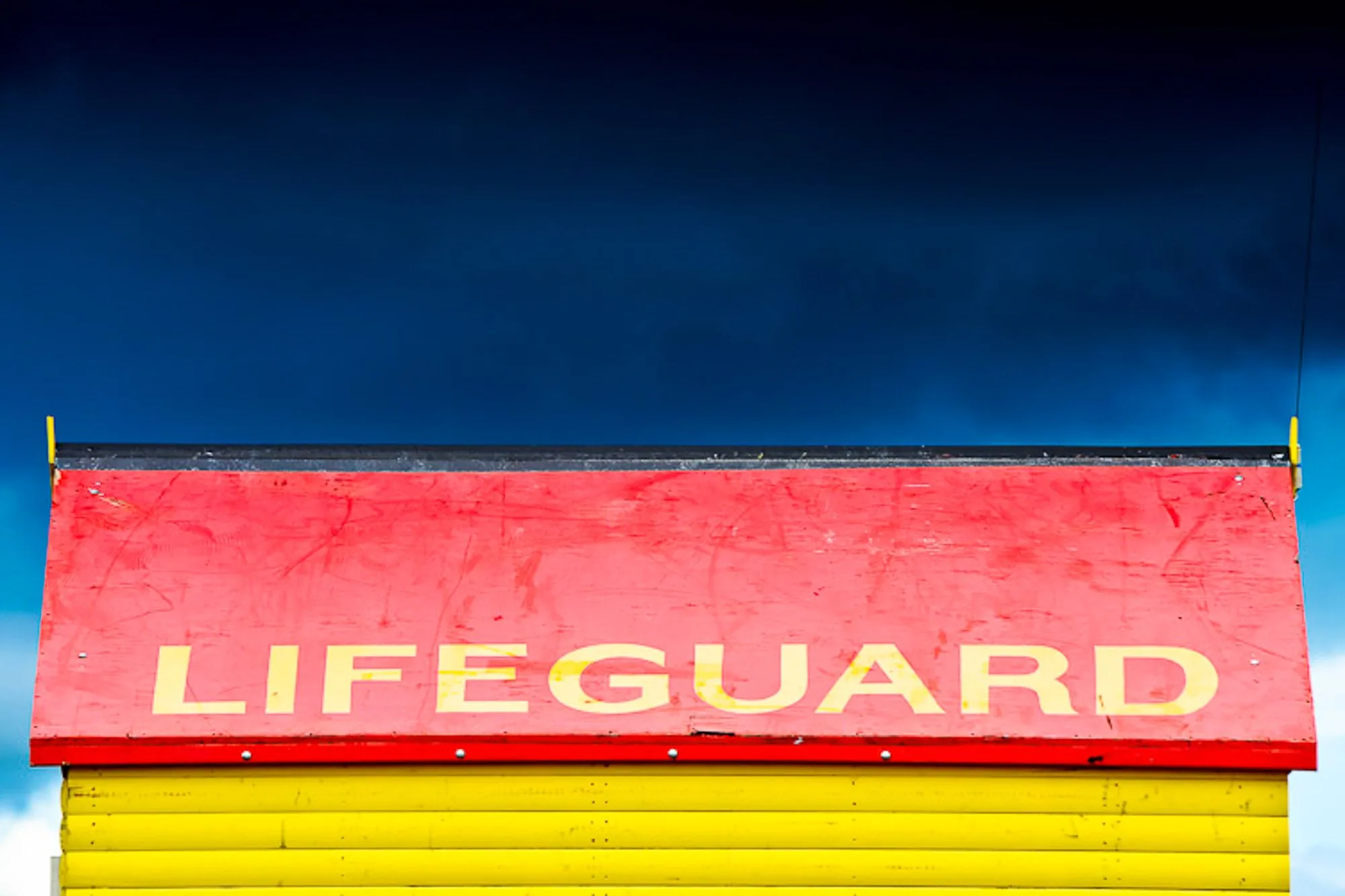 Red and yellow lifeguard hut roof sign against a deep blue sky