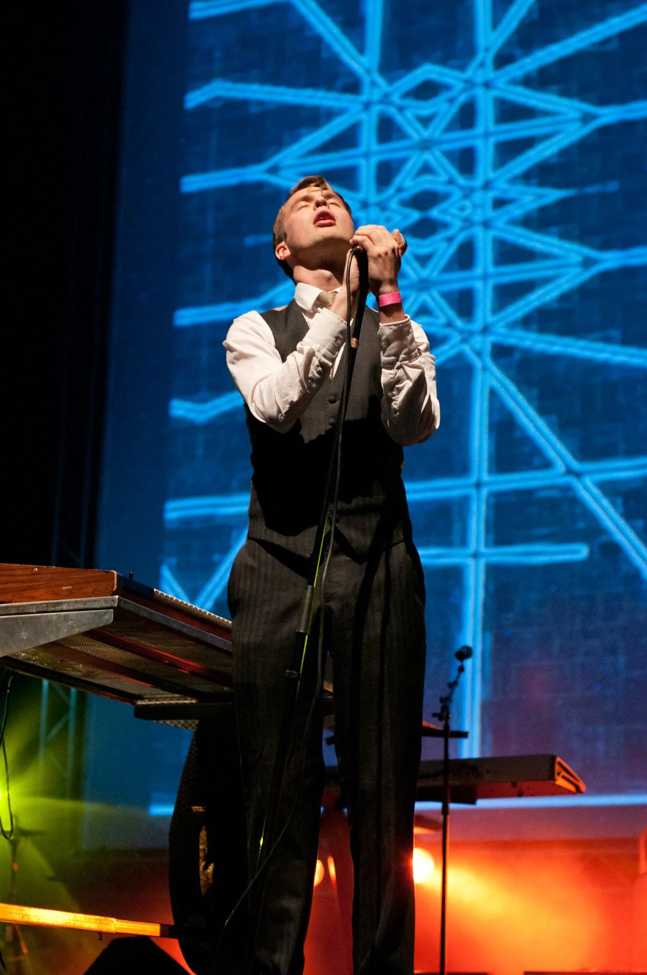 Singer performing on stage against a glowing blue geometric backdrop, live music photography by Hector's Eye