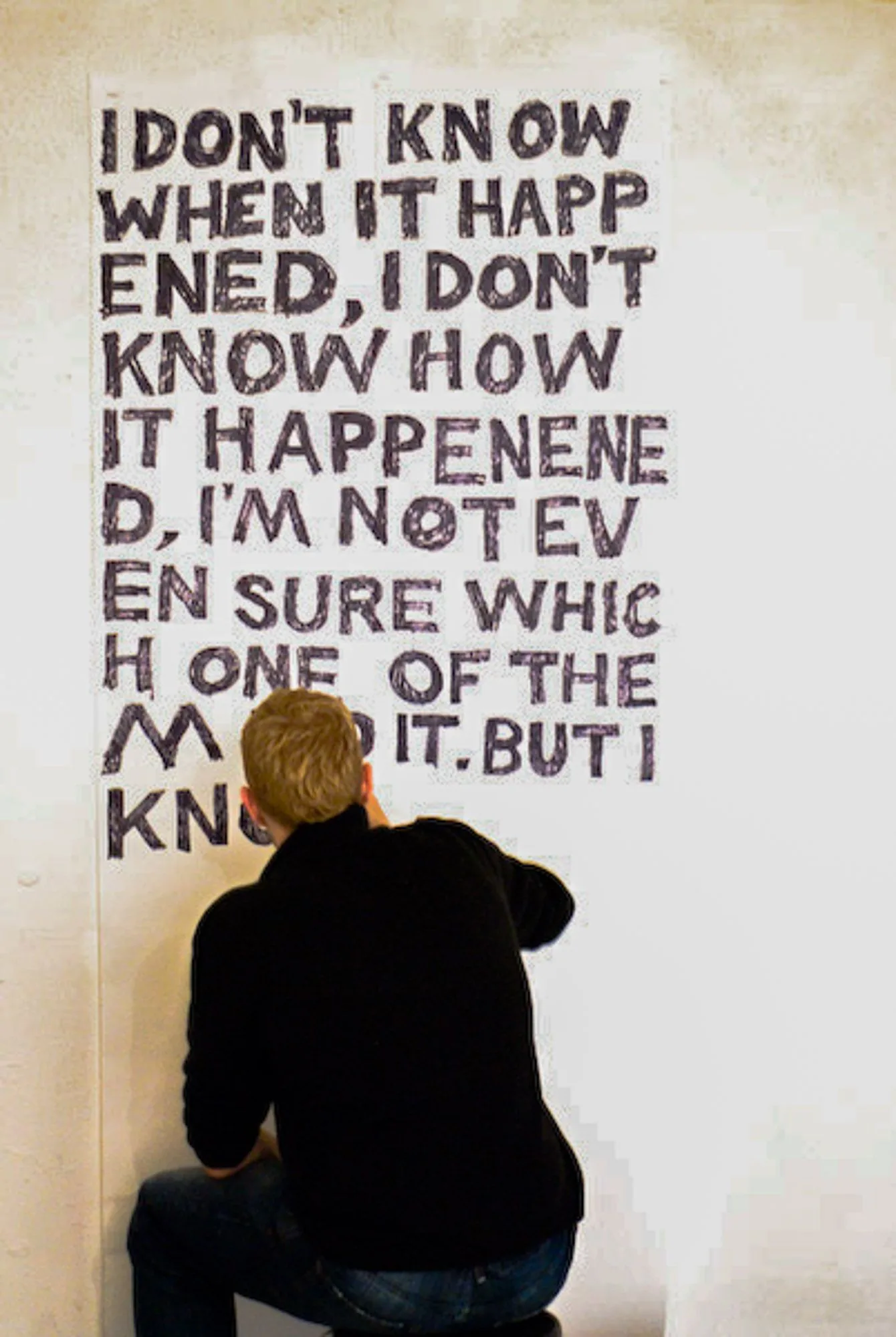 Artist hand-painting text onto a gallery wall at a live painting exhibition, live event photography by Hector's Eye