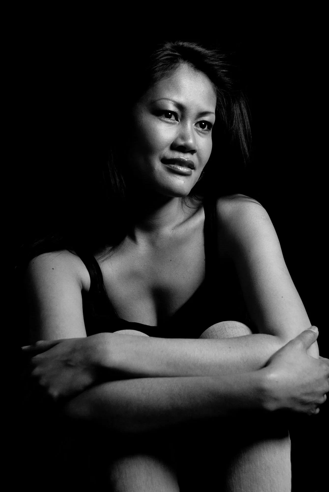 Moody black and white studio portrait of a woman seated with arms wrapped around her knees, editorial portrait photography by Hector's Eye