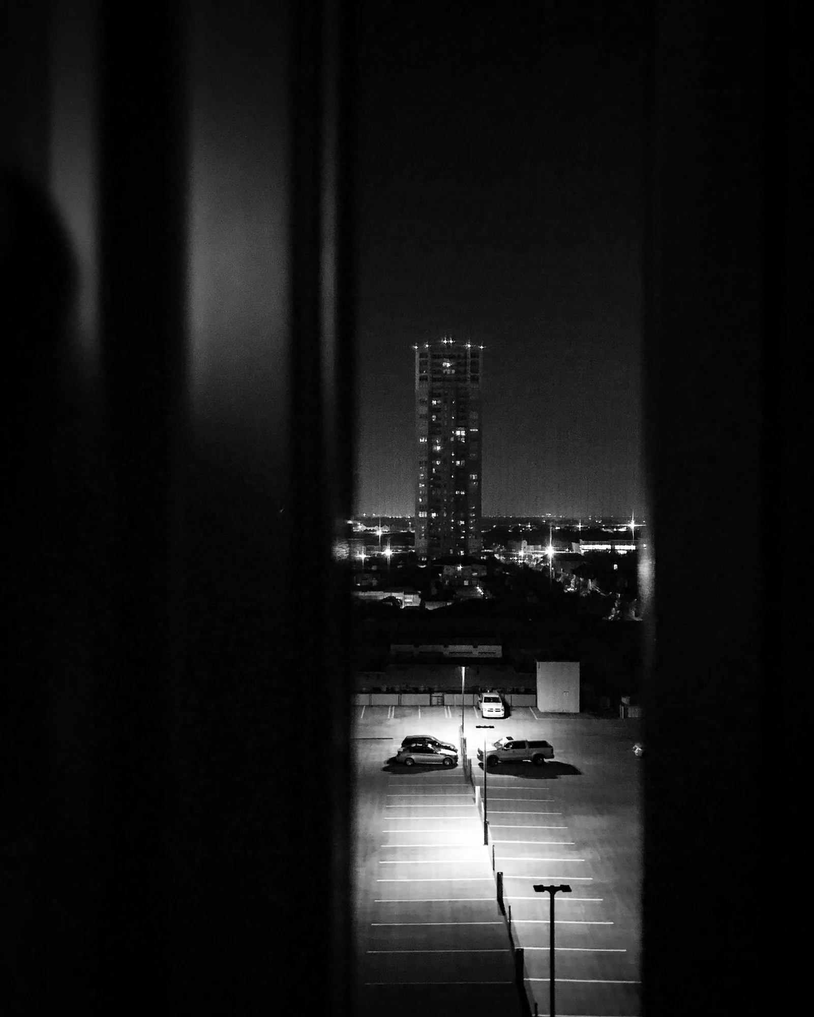 Night cityscape and empty car park seen through a gap in curtains