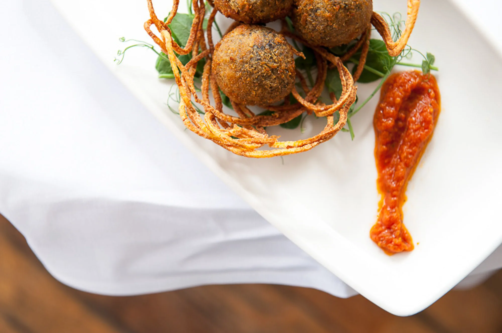 Overhead shot of fried arancini plated with pea shoots and tomato sauce, restaurant food photography by Hector's Eye