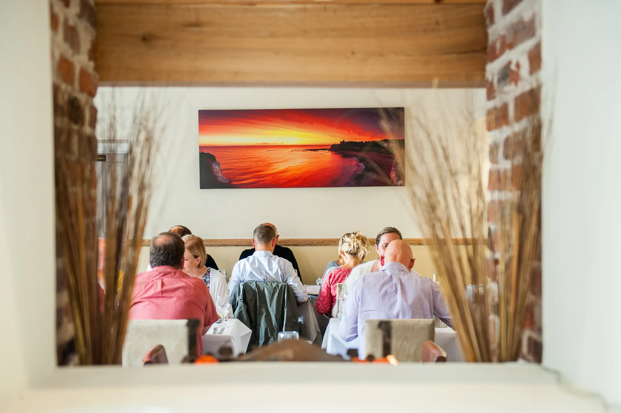 Diners seated beneath a sunset seascape canvas inside a restaurant, brand photography by Hector's Eye