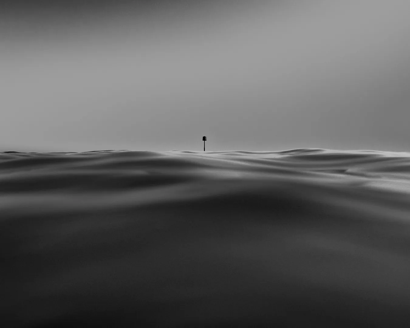 Lone sea marker buoy on the horizon line, black and white abstract photography by Hector's Eye