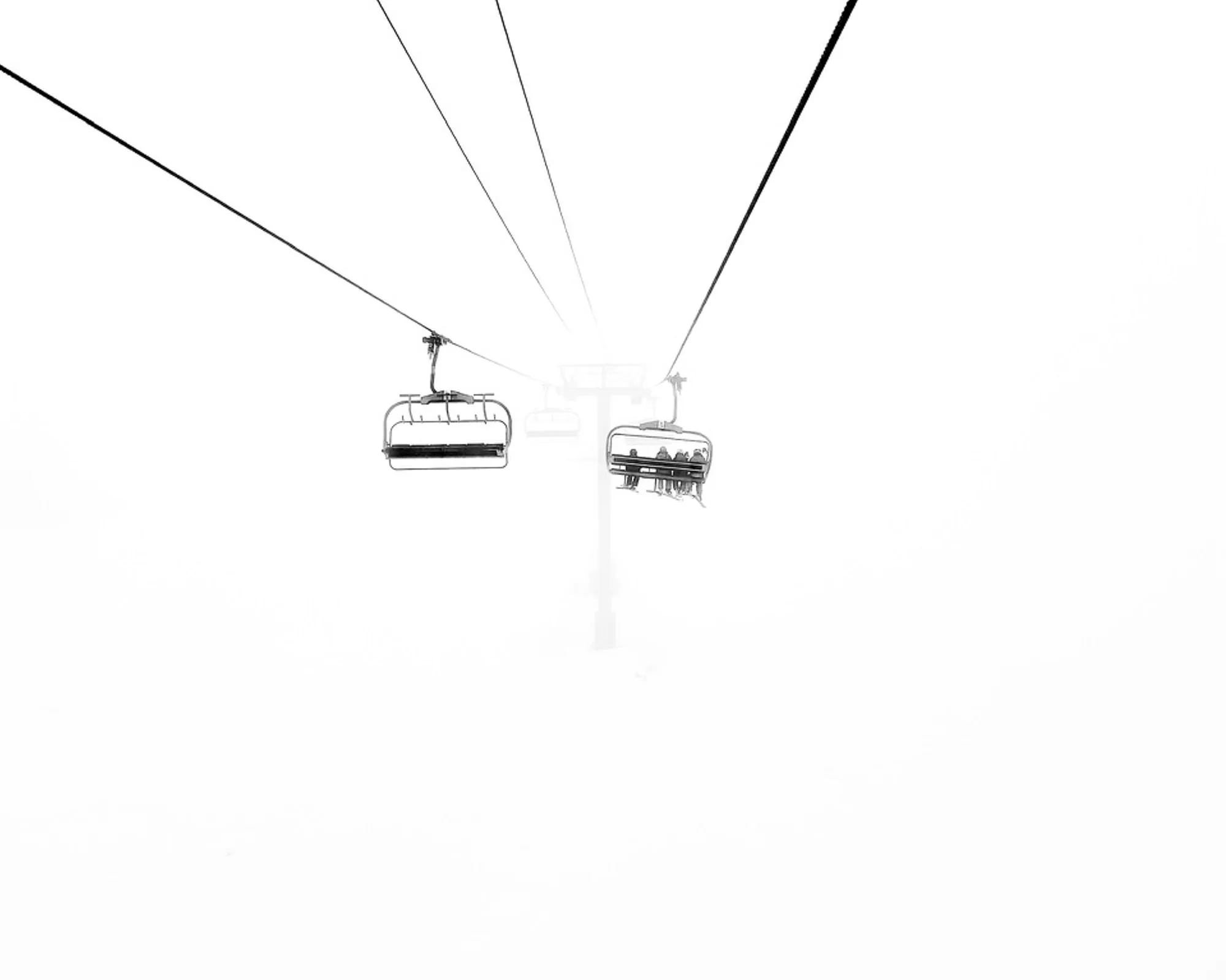 Ski chairlifts disappearing into thick white fog, minimalist black and white abstract photography