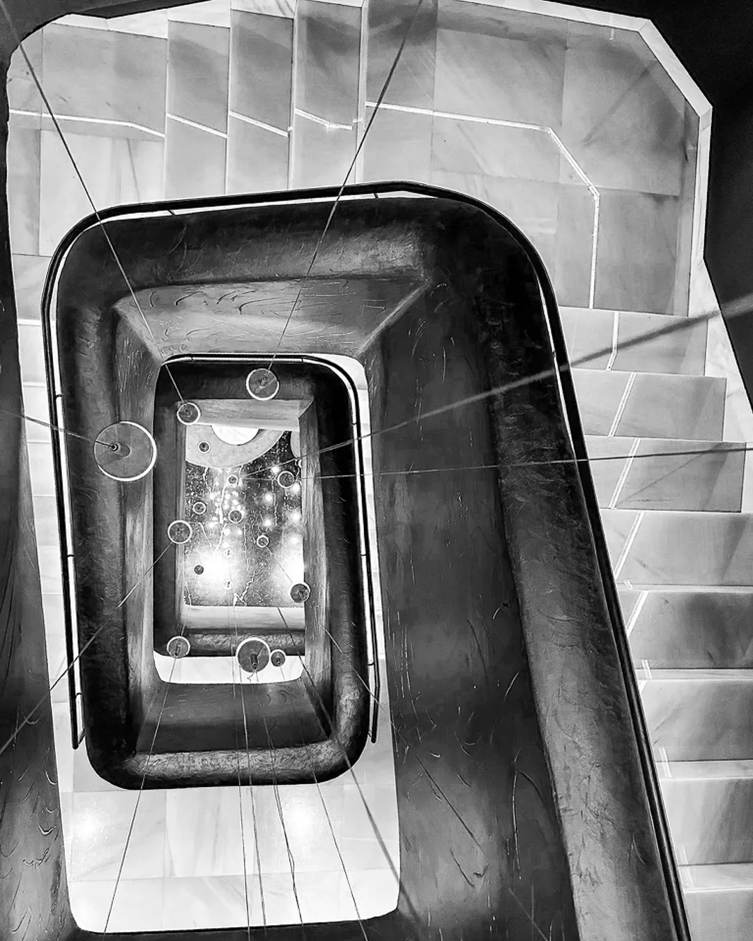 Looking down a spiral staircase atrium with hanging lights below