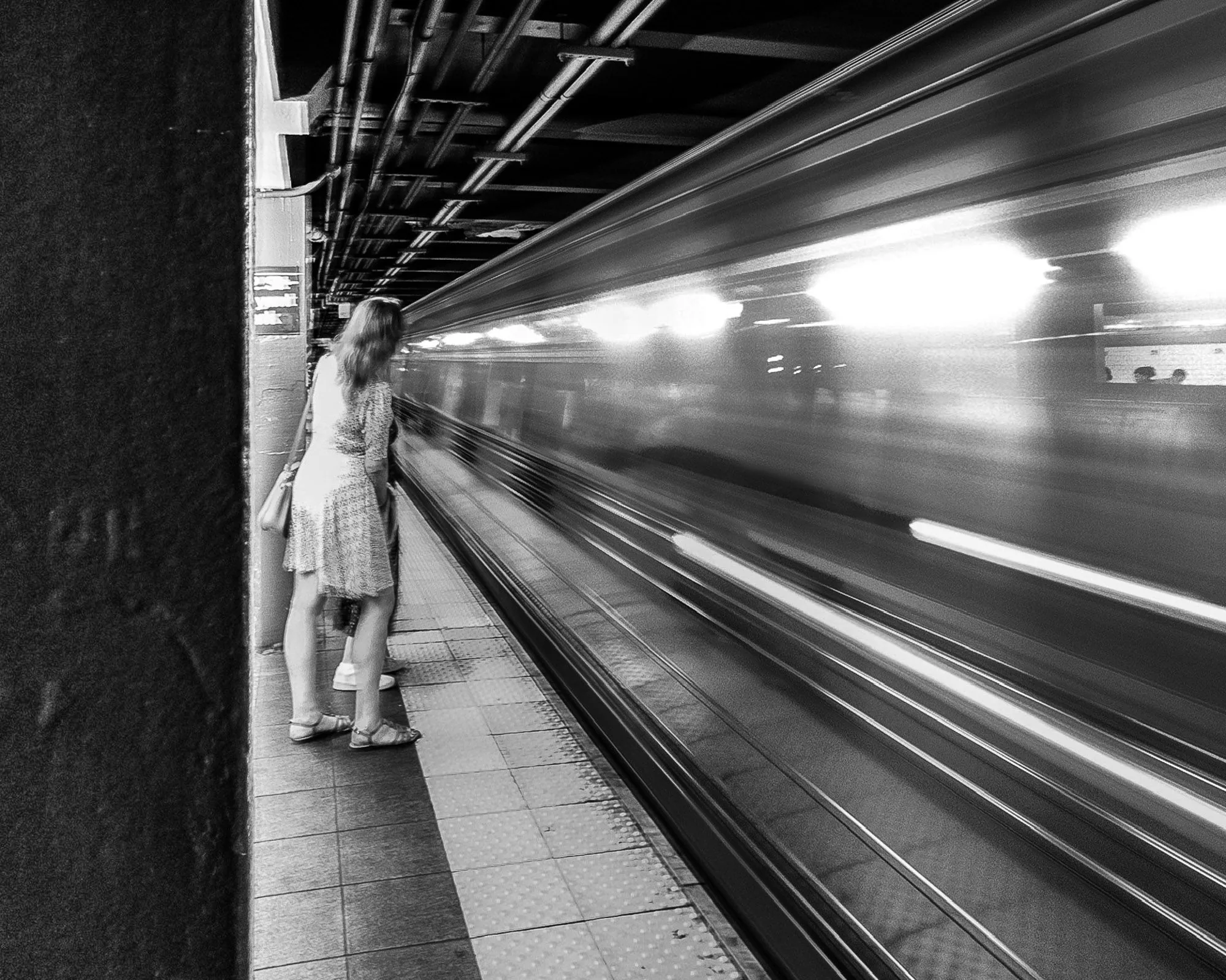 Woman waiting on a subway platform as a train speeds past in a long exposure, black and white photography