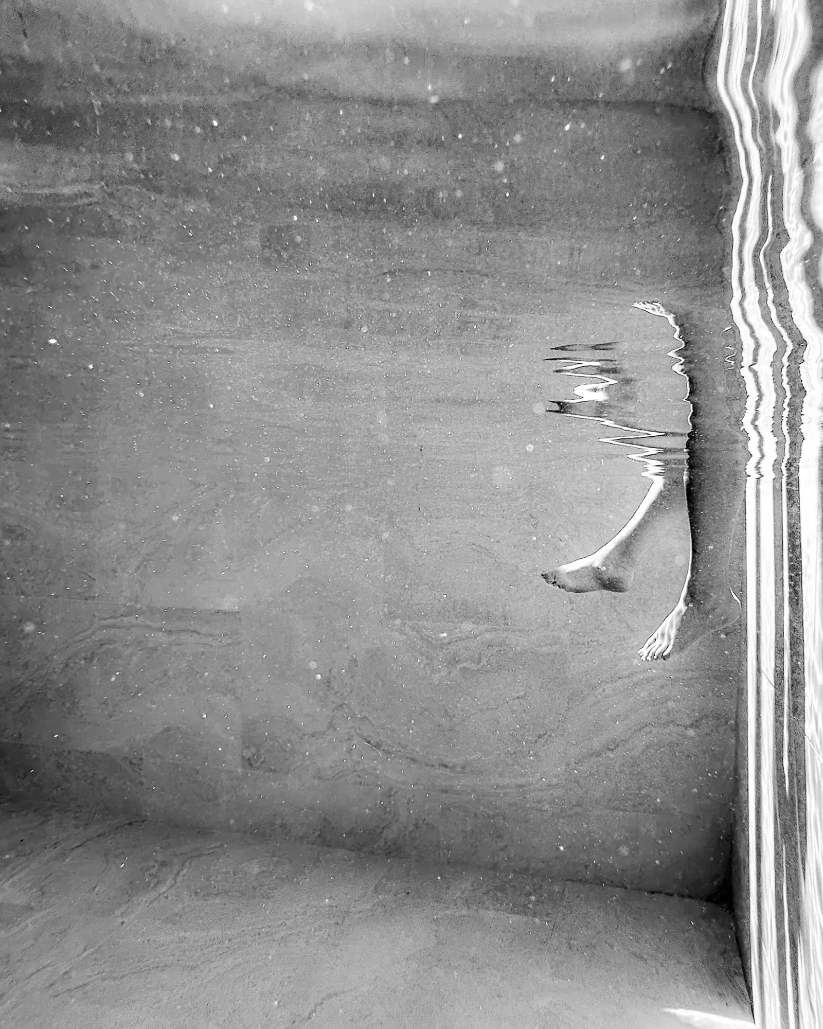 Legs of a swimmer breaking the surface reflection underwater, black and white abstract photography