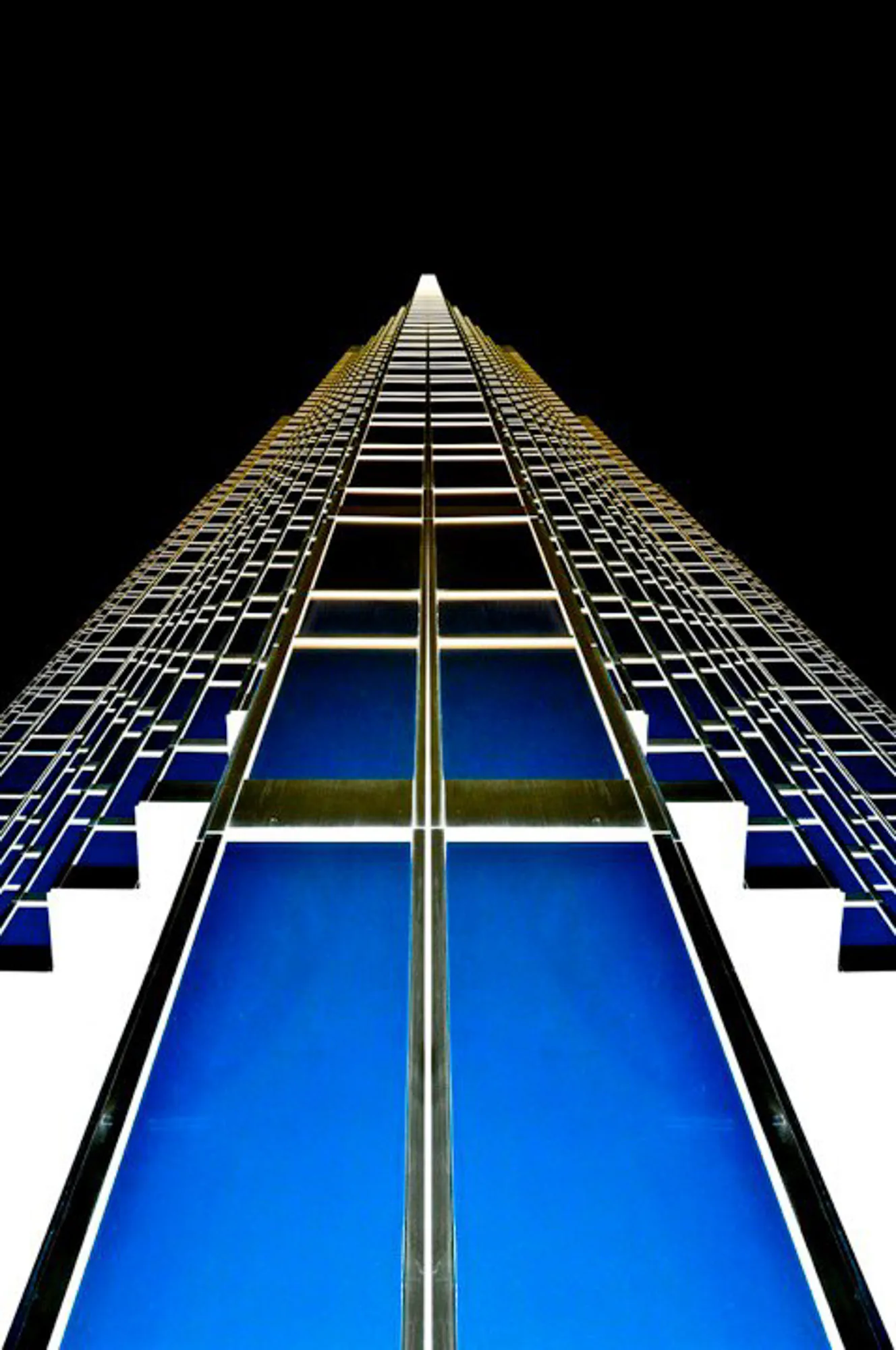 Symmetrical view looking straight up a blue-glass skyscraper against a black sky, abstract photography