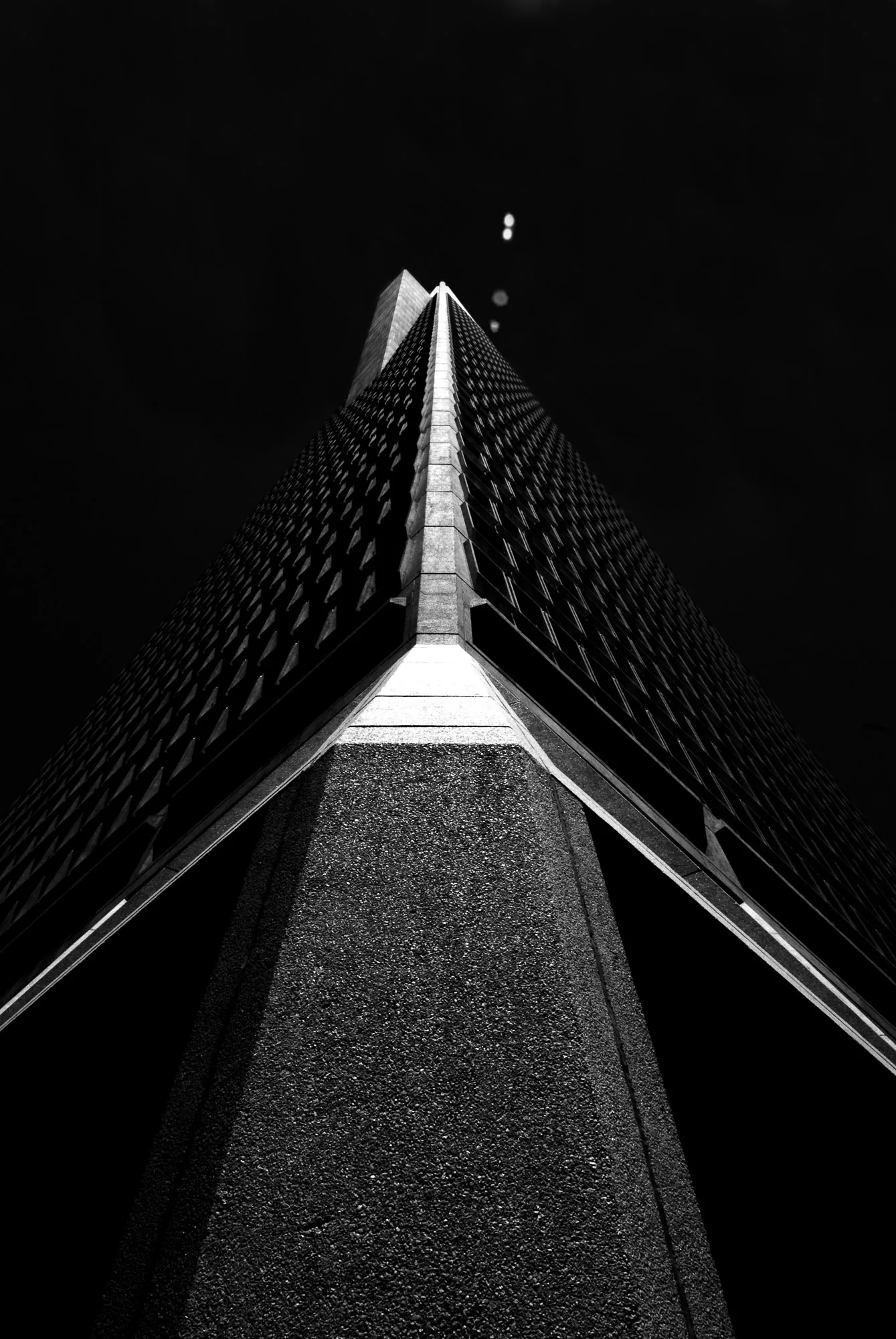 Symmetrical view looking up the corner edge of a building against a dark sky, black and white architectural photography by Hector's Eye