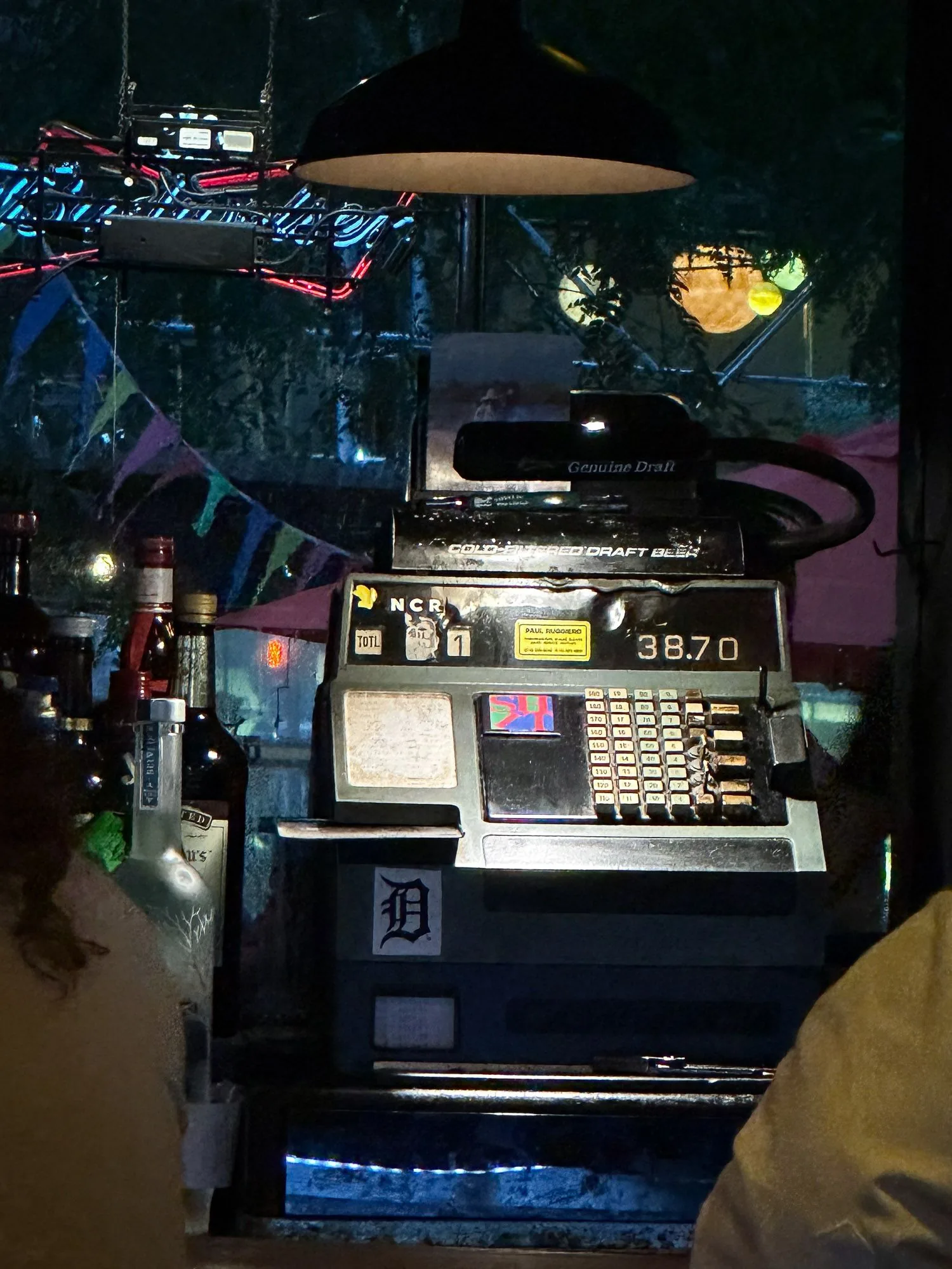 Vintage NCR cash register on a bar counter at night, string lights and bunting behind
