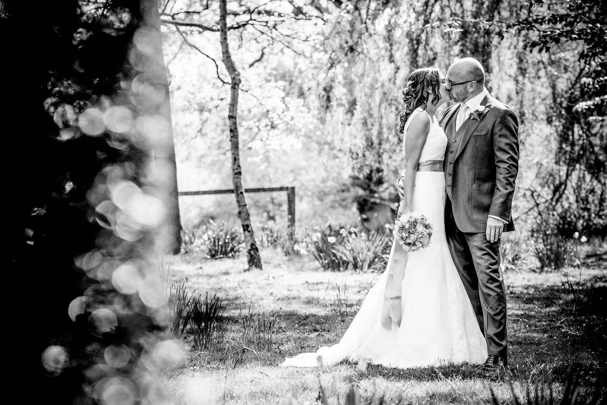 Bride and groom kissing in dappled woodland light, black and white wedding portrait photography by Hector's Eye
