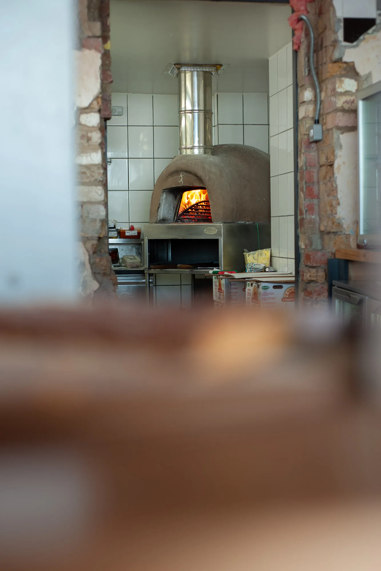Wood-fired pizza oven with flames visible through an exposed brick doorway, restaurant brand photography by Hector's Eye